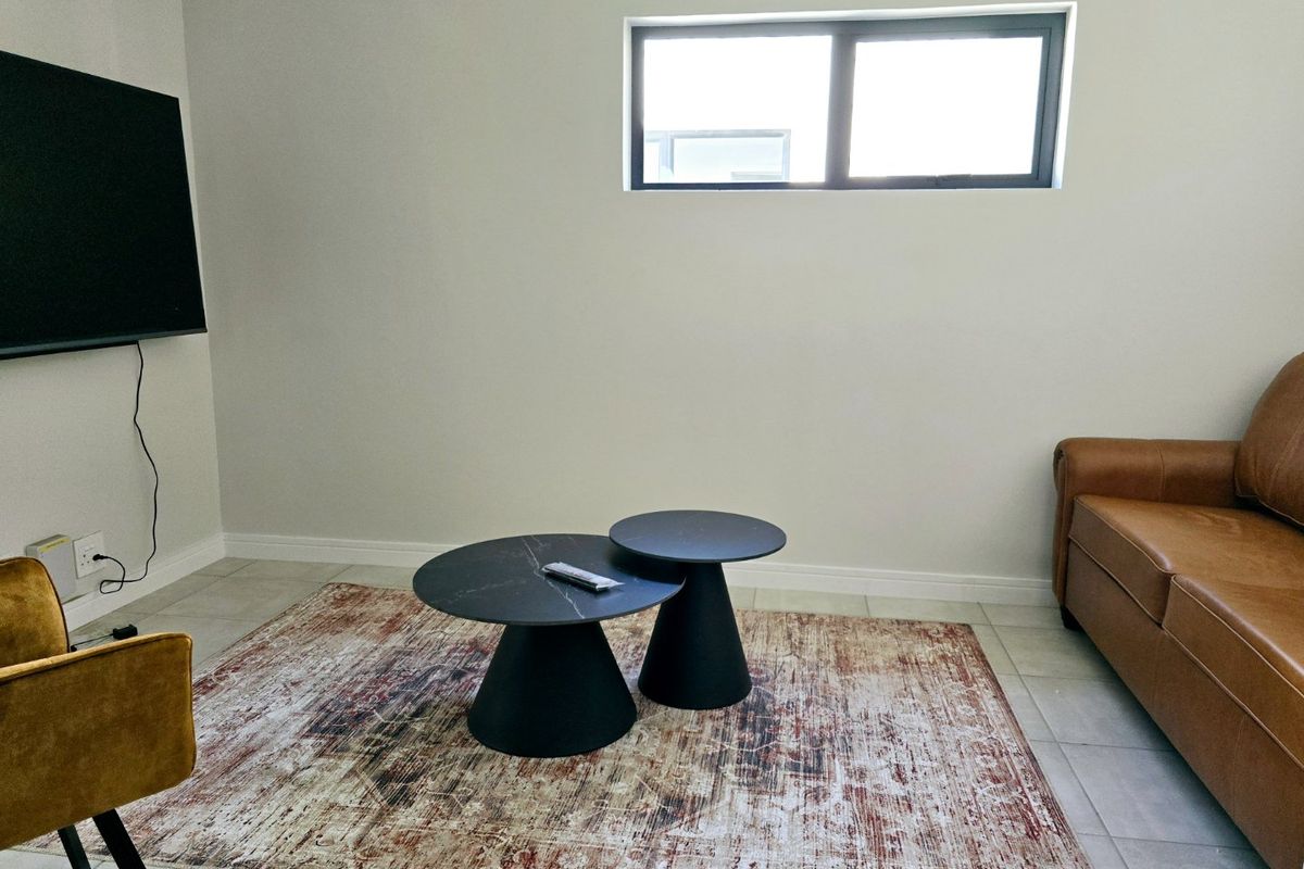 A modern living room featuring neutral walls, tiled flooring, and a horizontal window, providing a clean and bright space.