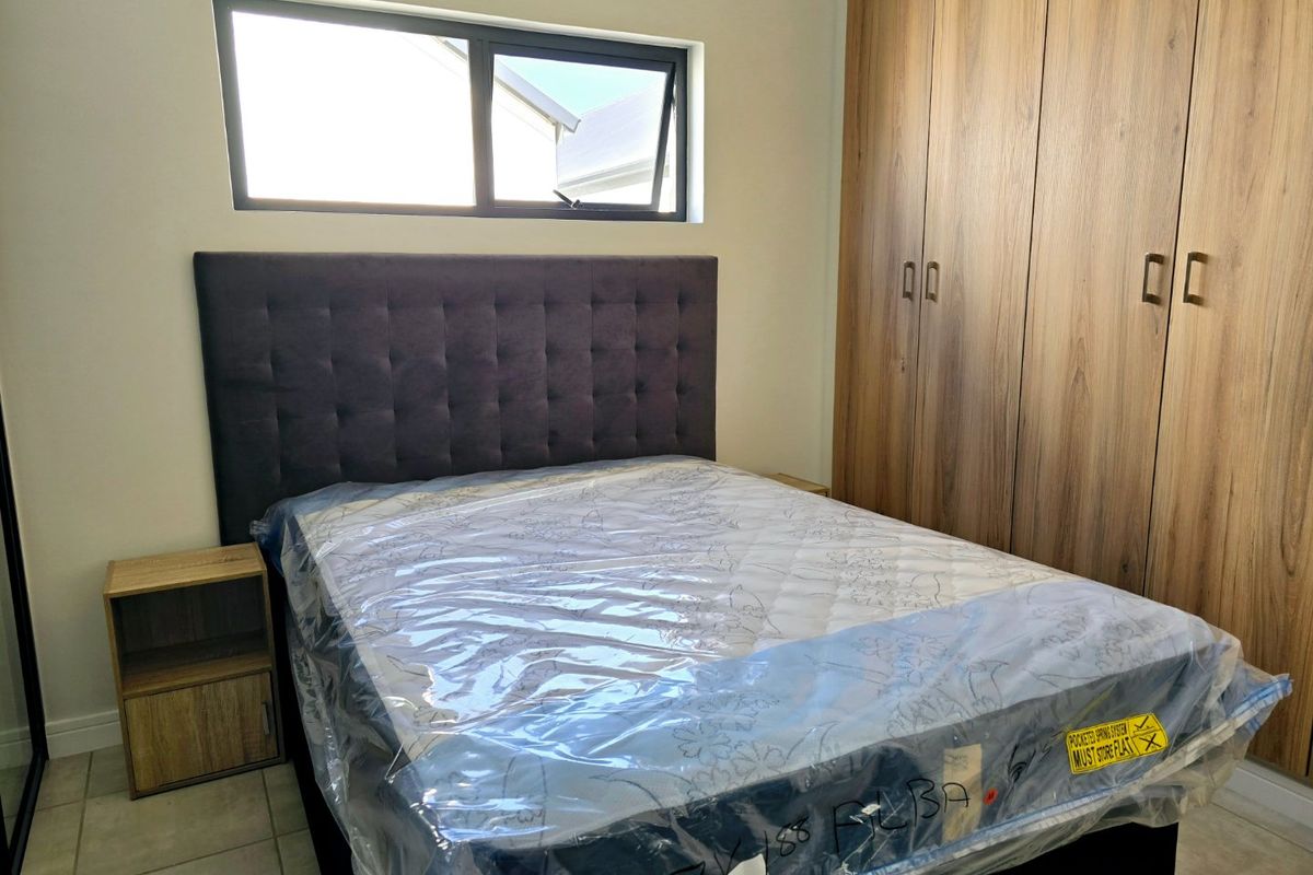 A modern bedroom featuring built-in wooden cupboards, tiled flooring, and a top-hung window, providing a clean and functional living space.