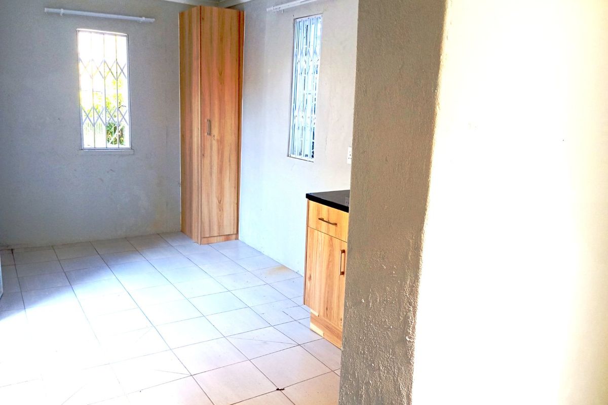 A functional kitchen area featuring tiled flooring, built-in cabinetry, and windows fitted with security bars.
