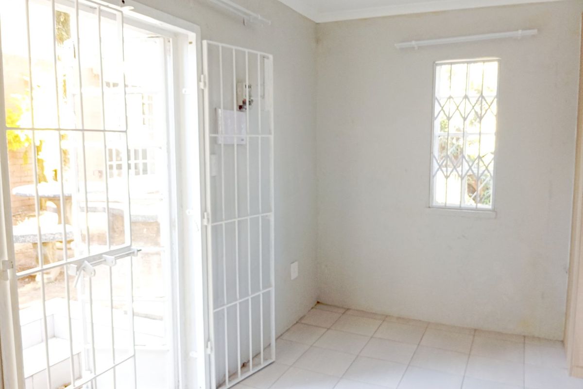 An empty, neutrally painted room featuring tiled flooring, a security gate at the entrance, and security bars on the window.