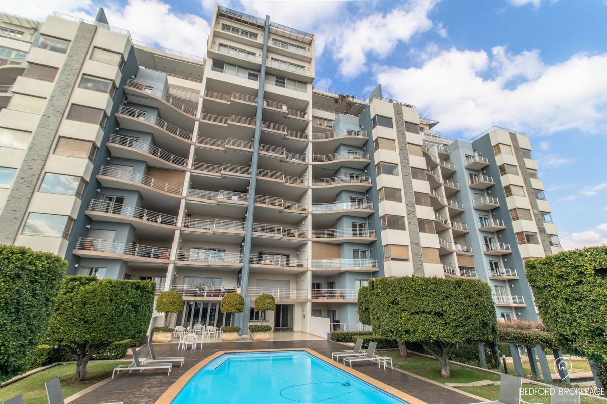 Rear view of a multi-story apartment complex featuring private balconies, a swimming pool, and landscaped garden areas.