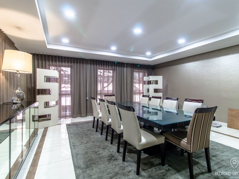 A spacious and elegant dining room featuring a tray ceiling with recessed lighting, polished tiled floors, and floor-to-ceiling curtains.