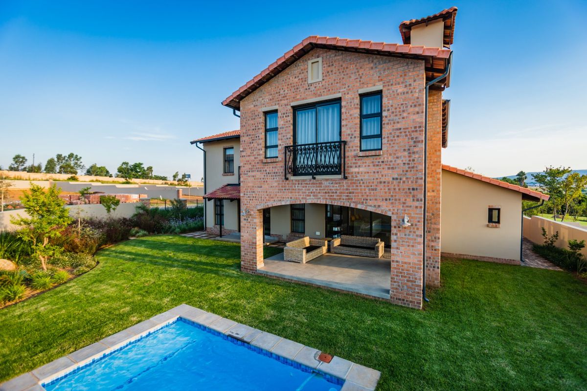 Rear view of a two-story brick residence featuring a covered patio, swimming pool, and well-maintained garden area.