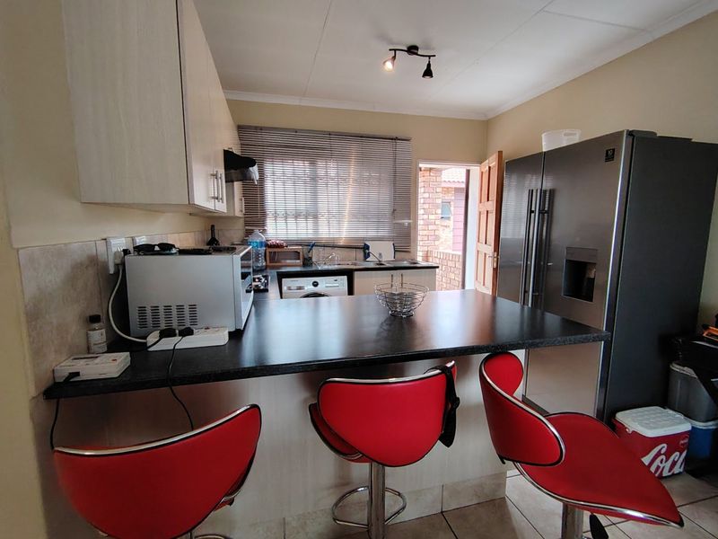 A functional kitchen featuring built-in cabinetry, a breakfast bar with a dark laminate countertop, tiled flooring, and direct access to an outdoor area.