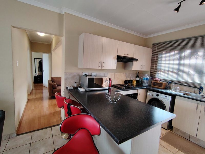 A functional kitchen featuring laminate cabinetry, a gas hob with extractor fan, and a breakfast counter, leading into a hallway.