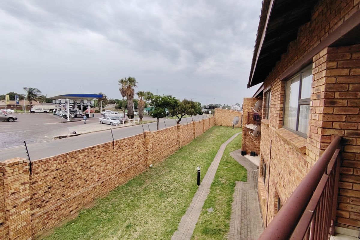 View of the rear exterior area featuring a face brick boundary wall with electric fencing, a paved walkway, and a small lawn.