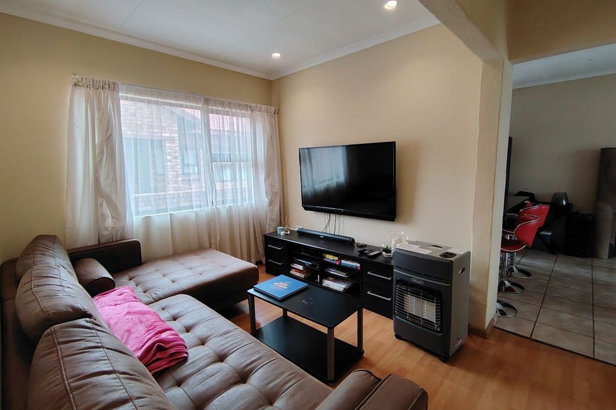 A comfortable living room featuring laminate flooring and recessed downlighting, with an open-plan layout connecting to the adjacent dining or kitchen area.