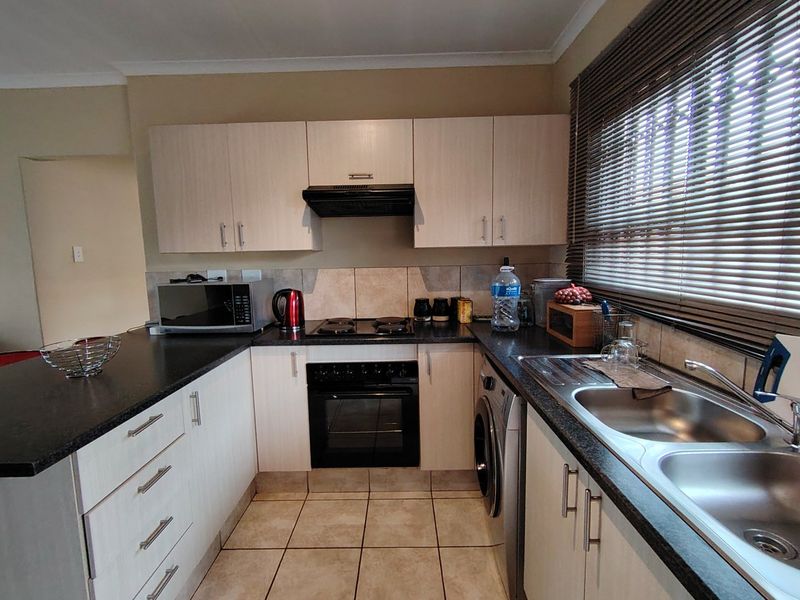 Functional kitchen featuring light wood-finish cabinetry, dark laminate countertops, integrated oven and hob, and a double stainless steel sink with tiled splashback.