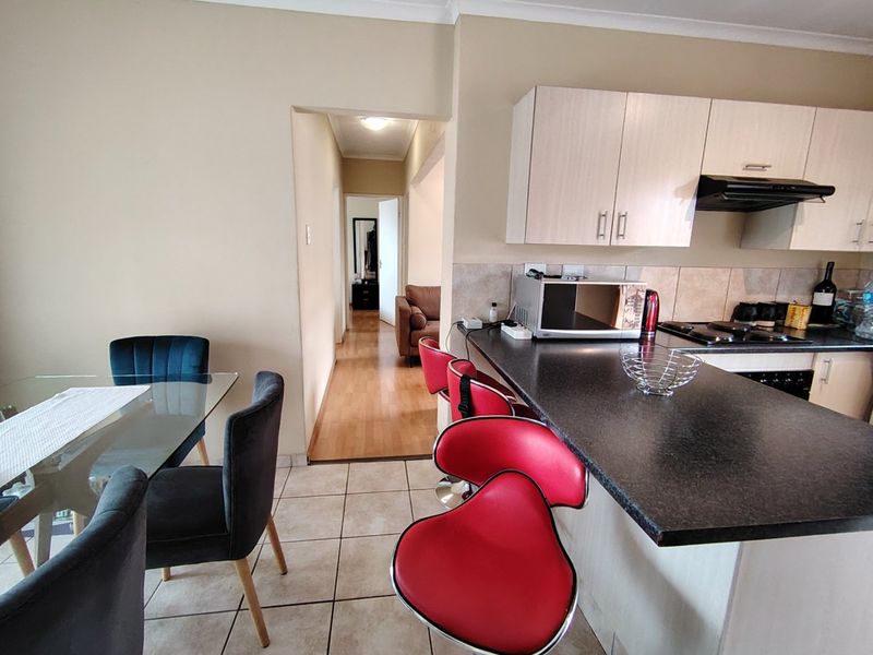 Open plan kitchen and dining area featuring laminate cabinetry, dark countertops, tiled flooring, and a breakfast bar, leading into a hallway.