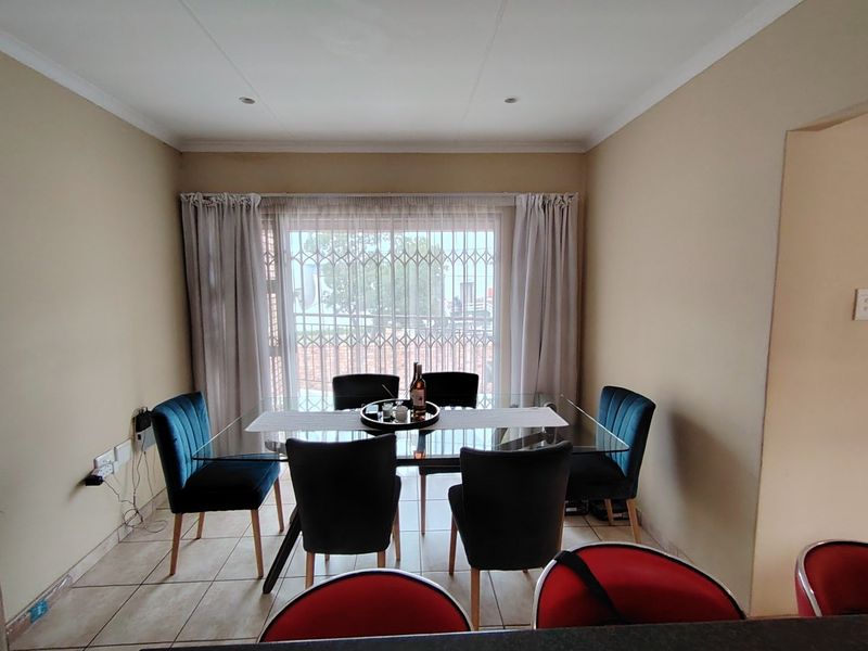 A functional dining area featuring tiled flooring, recessed lighting, and a large window with a security gate, providing a bright and practical space.