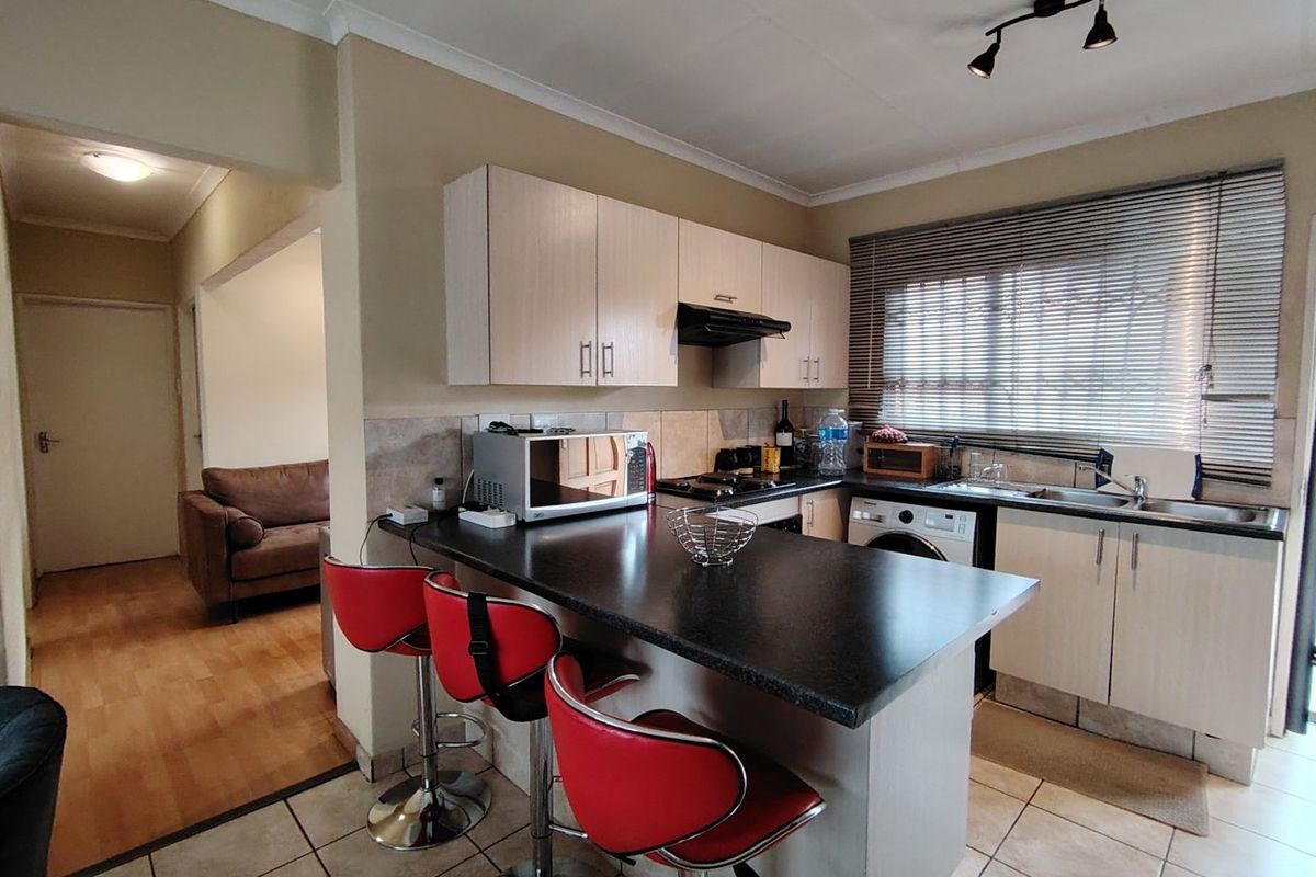 A functional kitchen featuring light-toned cabinetry, dark laminate countertops, a breakfast bar, and tiled flooring, with an adjacent view into the living area.