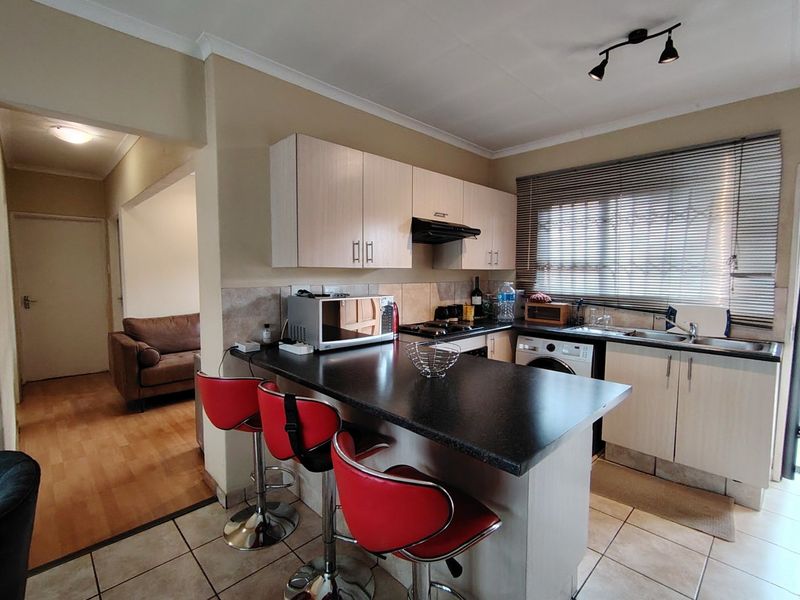 A functional kitchen featuring light-toned cabinetry, dark laminate countertops, a breakfast bar, and tiled flooring, with an adjacent view into the living area.