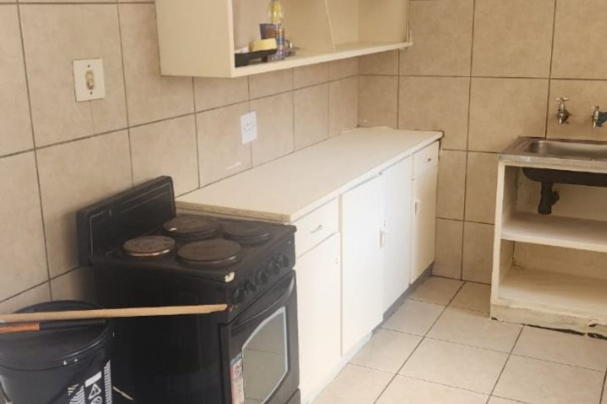 A functional kitchen space featuring tiled flooring, a stainless steel sink, built-in cabinetry, and a freestanding stove, offering potential for modernization and cosmetic updates.