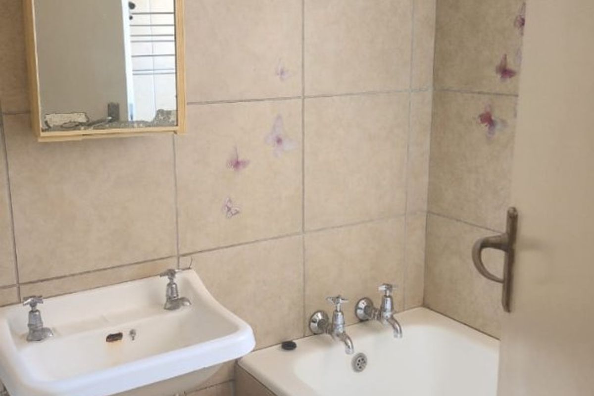 A dated bathroom featuring a wall-mounted water heater, ceramic tiling, a standard basin, and a built-in bathtub, requiring significant cosmetic updates and maintenance.