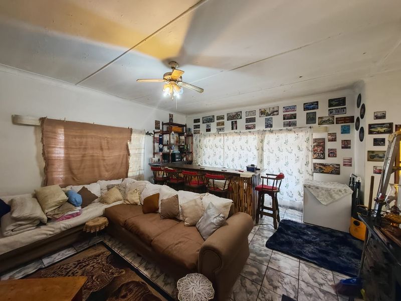 Open plan living area featuring a built-in bar counter, tiled flooring, and a ceiling fan, offering potential for modernization and layout optimization.