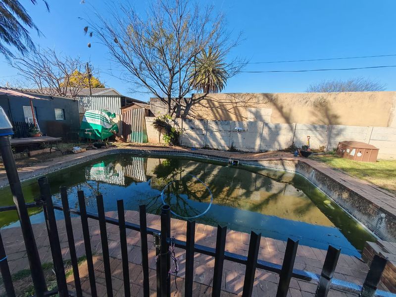 Outdoor pool area featuring a swimming pool with brick paving, enclosed by a metal security fence and a precast concrete boundary wall.