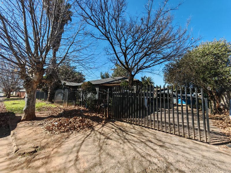 Front view of the property featuring a metal security gate, driveway access, and mature trees along the street frontage.