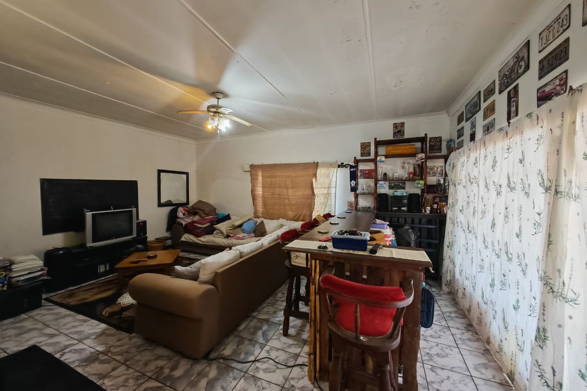 A living room area featuring tiled flooring and a ceiling fan, showing signs of wear and requiring cosmetic updates to the ceiling.