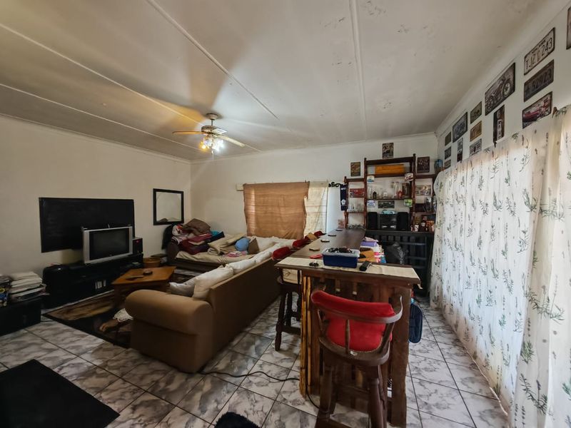 A living room area featuring tiled flooring and a ceiling fan, showing signs of wear and requiring cosmetic updates to the ceiling.