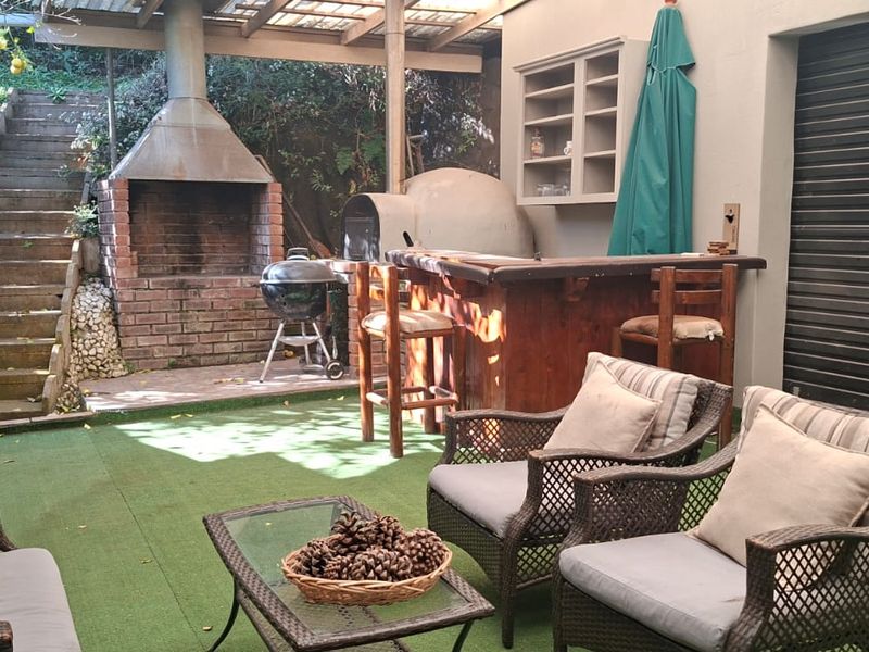 Outdoor entertainment area featuring a built-in brick braai, pizza oven, pergola cover, and direct access to garden stairs.