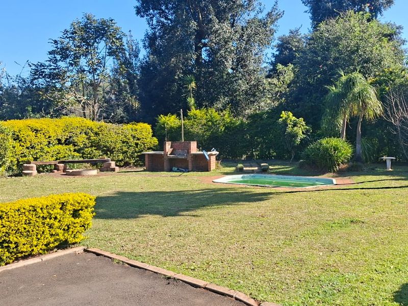 Spacious backyard featuring a swimming pool, a brick built-in braai area, and established garden landscaping.