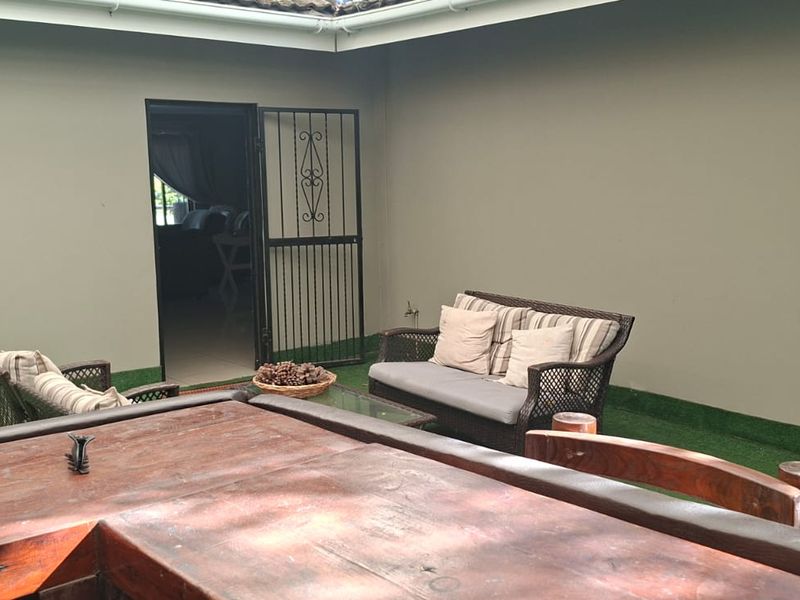 A covered outdoor patio area featuring artificial turf flooring, a security gate, and a solid timber door providing access to the interior.