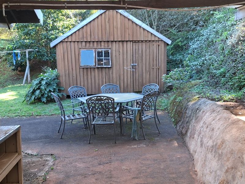 A covered outdoor patio area featuring a built-in sink, a rustic retaining wall, and a separate wooden storage shed in the garden.