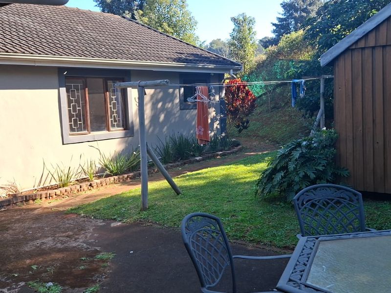 Rear exterior view of the property featuring a concrete patio, lawn area, and a detached wooden outbuilding.