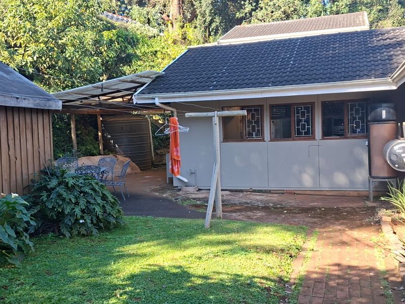 Rear exterior view of the property featuring a paved walkway, lawn area, water tank, and external geyser installation.