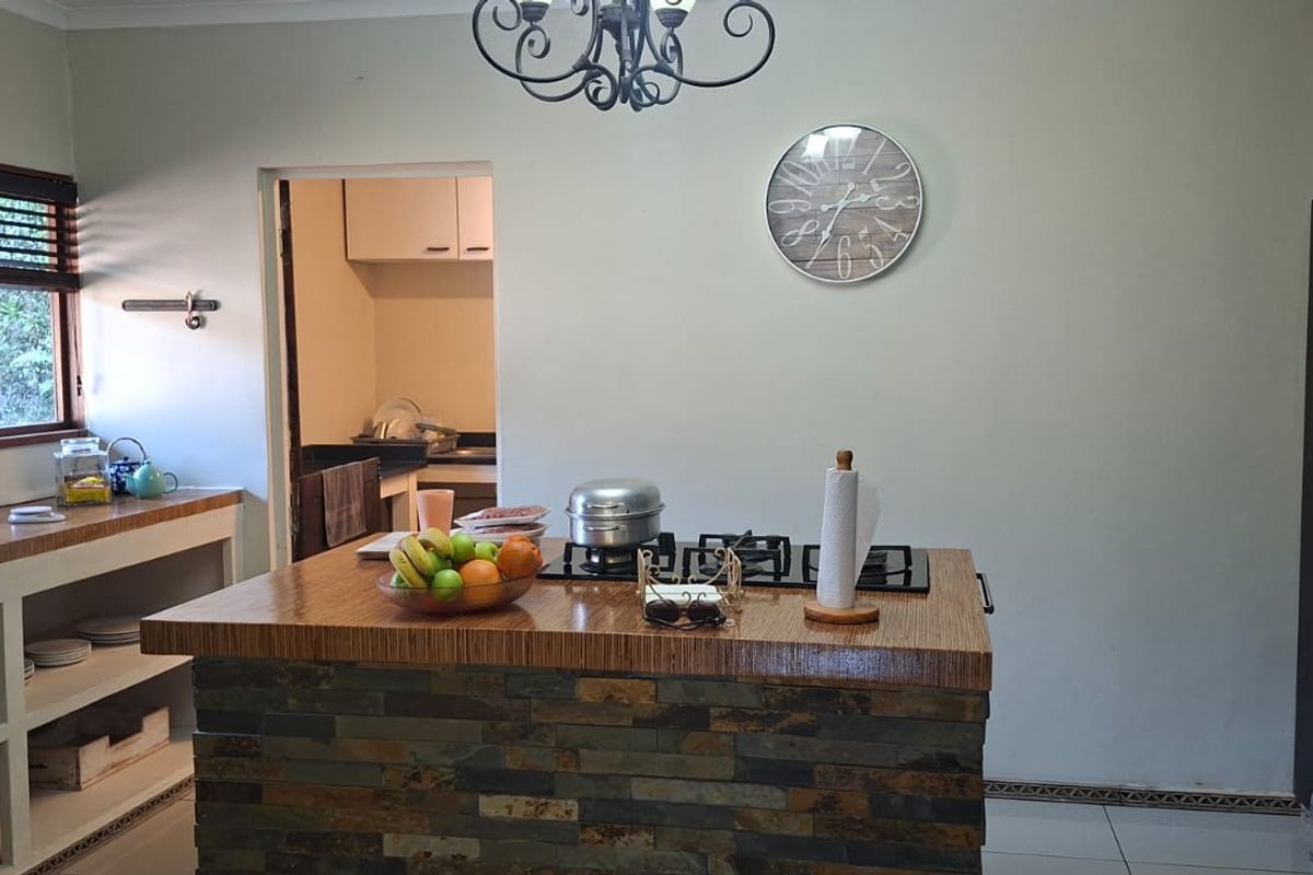 Kitchen featuring a central island with stone veneer finish, built-in gas hob, double oven, and open shelving, with an adjacent scullery area.