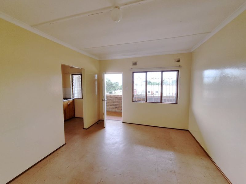 An empty open-plan living area featuring vinyl flooring, security bars on windows, and direct access to an outdoor balcony area.