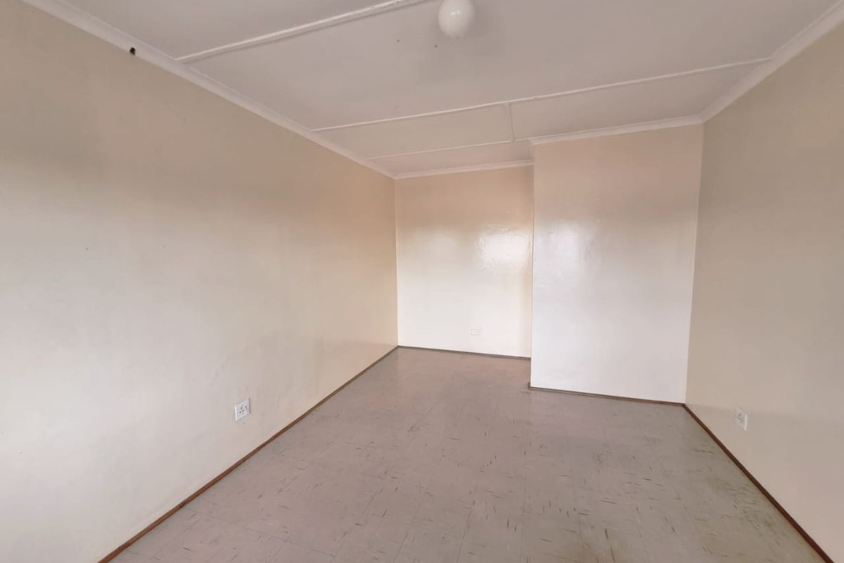 An empty, neutrally painted living area featuring tiled flooring and basic electrical fixtures, offering a blank canvas for potential interior design updates.
