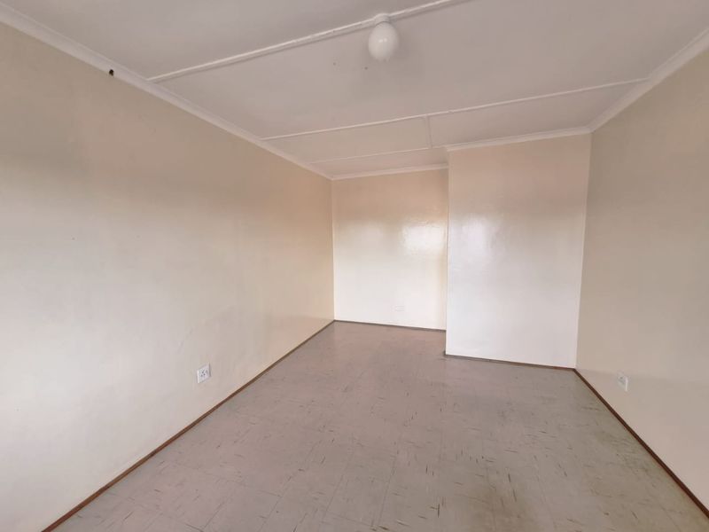 An empty, neutrally painted living area featuring tiled flooring and basic electrical fixtures, offering a blank canvas for potential interior design updates.