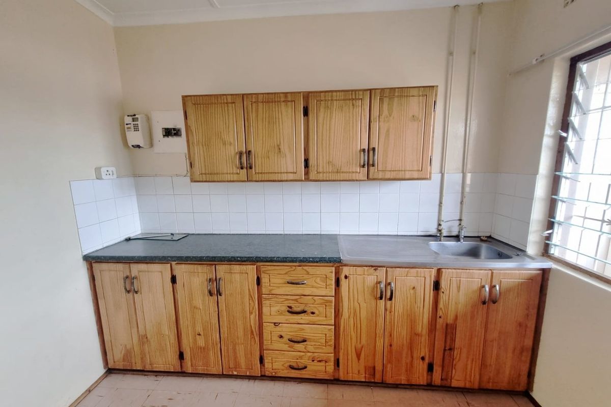 A functional kitchen area featuring wooden cabinetry, a stainless steel sink, and tiled backsplash, offering a blank canvas for potential modern updates.