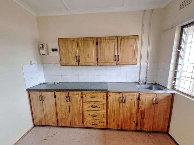 A functional kitchen area featuring wooden cabinetry, a stainless steel sink, and tiled backsplash, offering a blank canvas for potential modern updates.