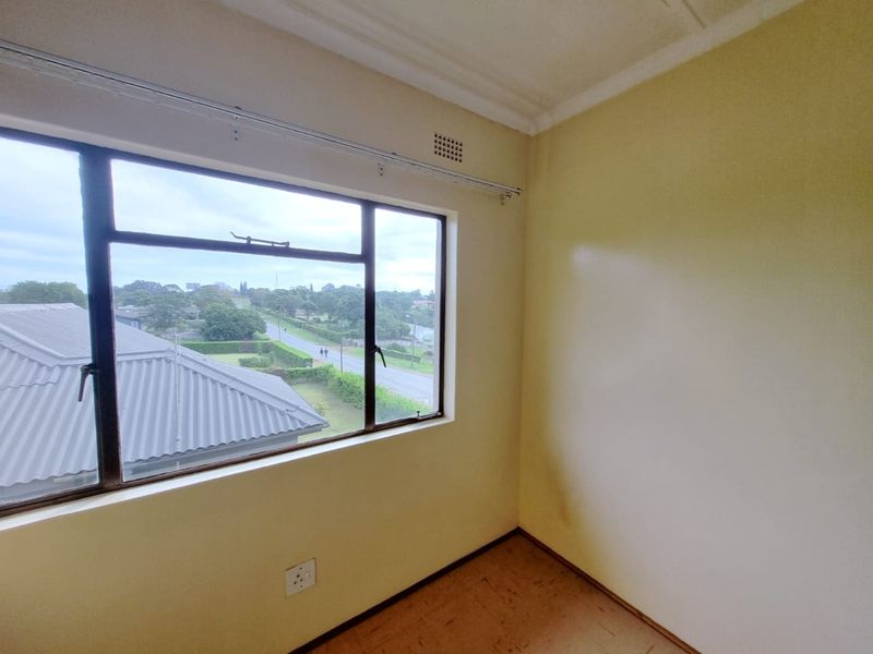 An empty bedroom featuring a metal frame window with exterior views, neutral walls, and worn flooring, ready for renovation or staging.