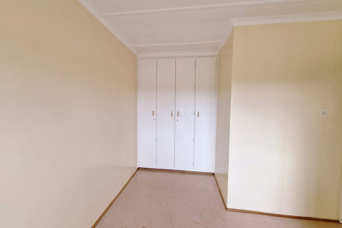 An empty bedroom featuring neutral walls, tiled flooring, and white built-in cupboards with a coved ceiling.