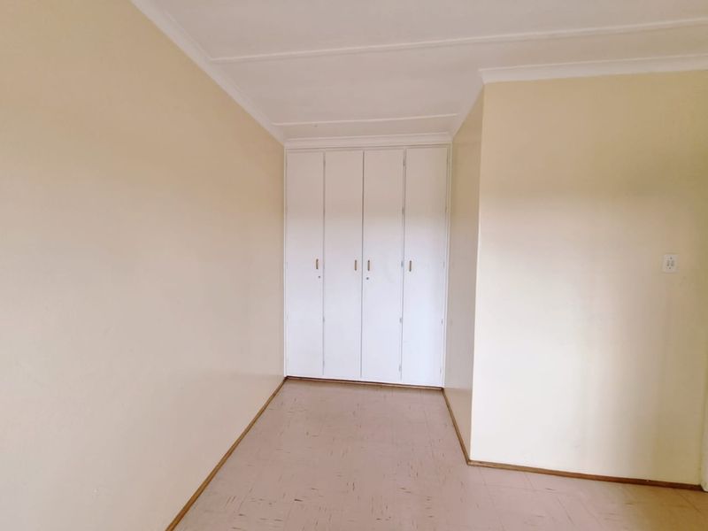 An empty bedroom featuring neutral walls, tiled flooring, and white built-in cupboards with a coved ceiling.