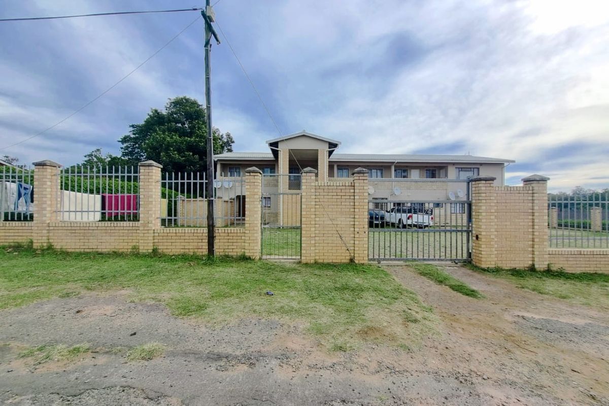 Front elevation of a multi-unit apartment building featuring a brick perimeter wall, metal security fencing, and a gated entrance.
