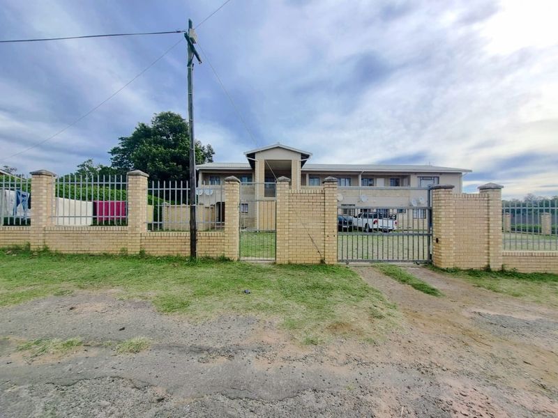 Front elevation of a multi-unit apartment building featuring a brick perimeter wall, metal security fencing, and a gated entrance.