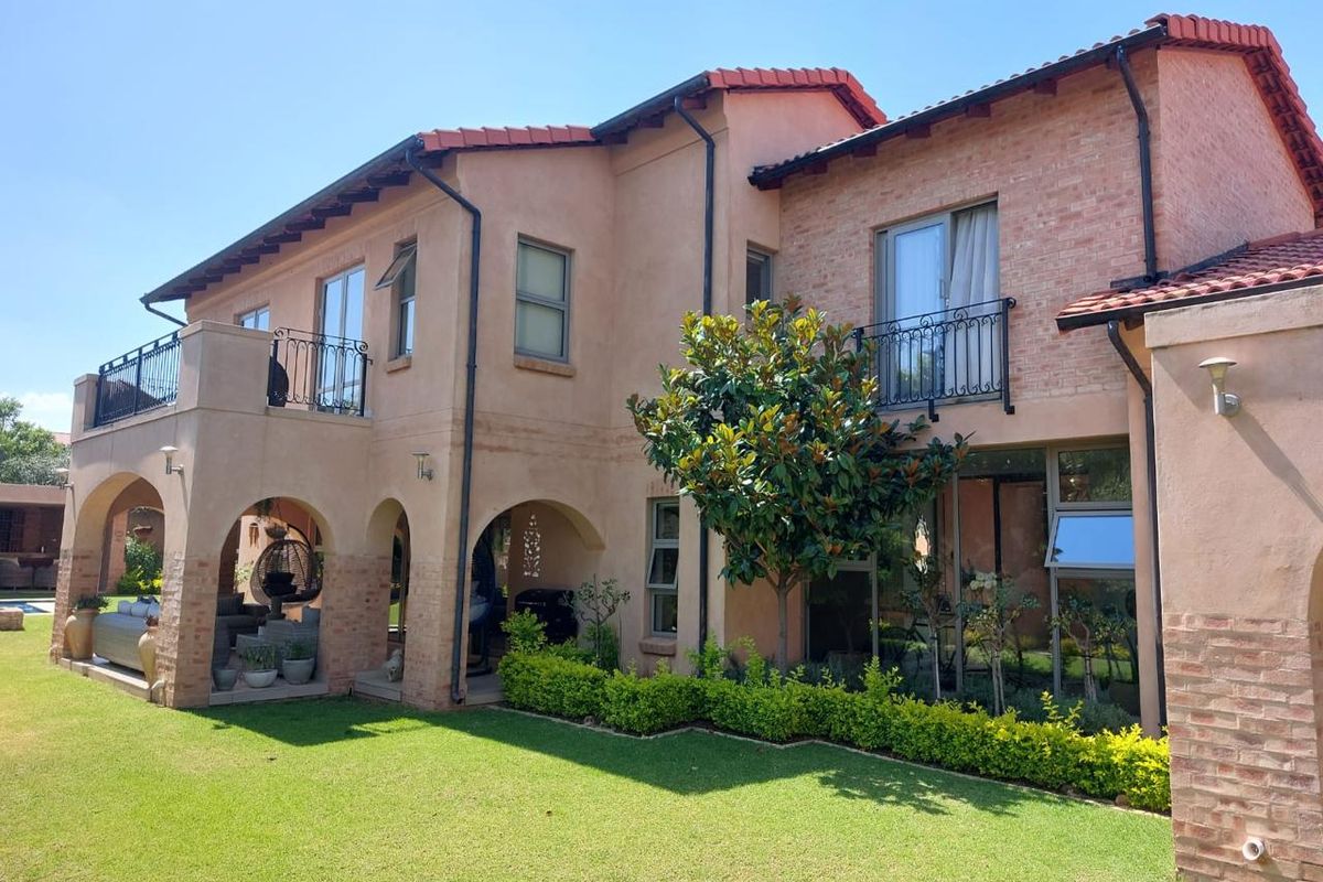 Rear view of a two-story house featuring a covered arched patio, upper-level balconies with wrought iron railings, and a well-maintained garden.