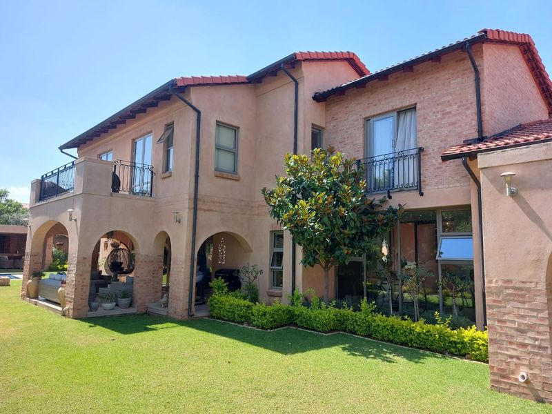 Rear view of a two-story house featuring a covered arched patio, upper-level balconies with wrought iron railings, and a well-maintained garden.