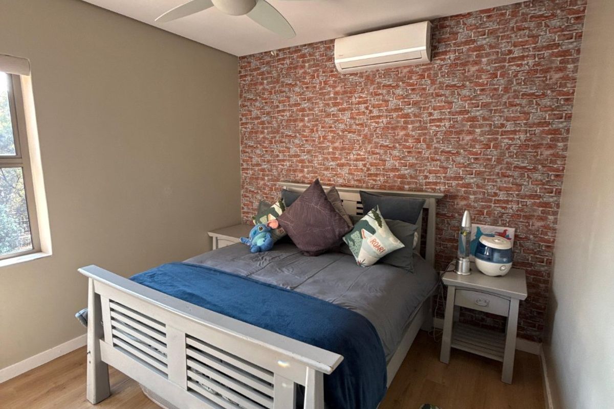 A well-maintained bedroom featuring a ceiling fan, split-system air conditioning, laminate flooring, and a decorative brick-effect feature wall.