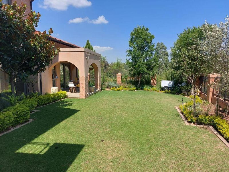 A well-maintained rear garden featuring a manicured lawn, established landscaping, and a covered patio with distinctive arched architectural detailing.