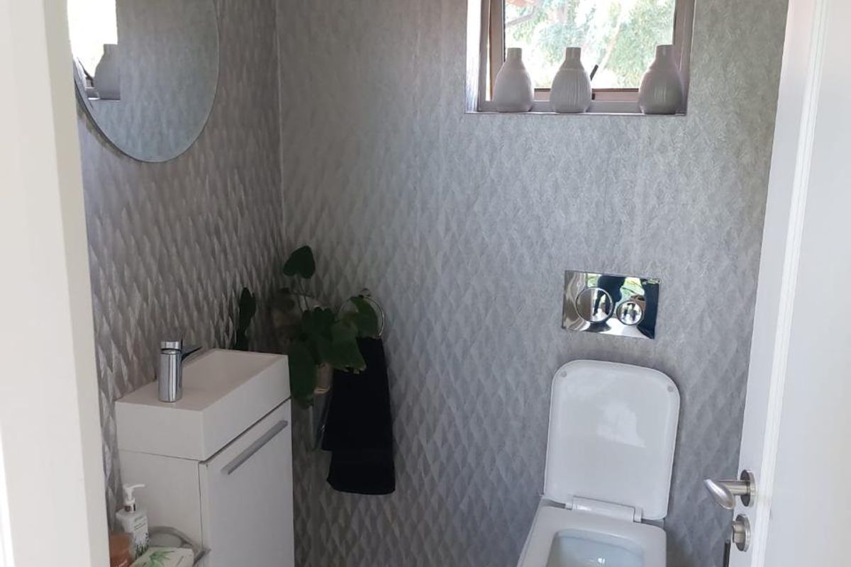 A compact, modern guest bathroom featuring a wall-mounted toilet, vanity basin with chrome fixtures, and contemporary textured wall tiling.