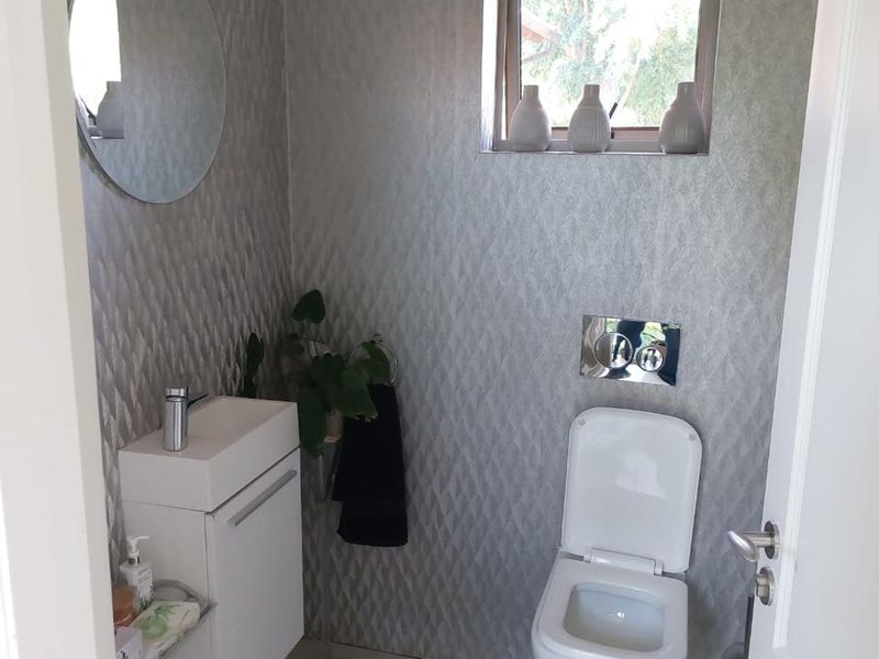 A compact, modern guest bathroom featuring a wall-mounted toilet, vanity basin with chrome fixtures, and contemporary textured wall tiling.