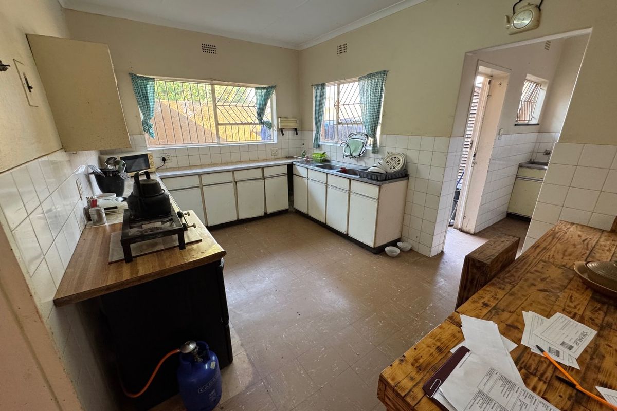 A functional kitchen featuring original cabinetry, tiled splashbacks, and a secondary scullery area, offering potential for modernization and renovation.