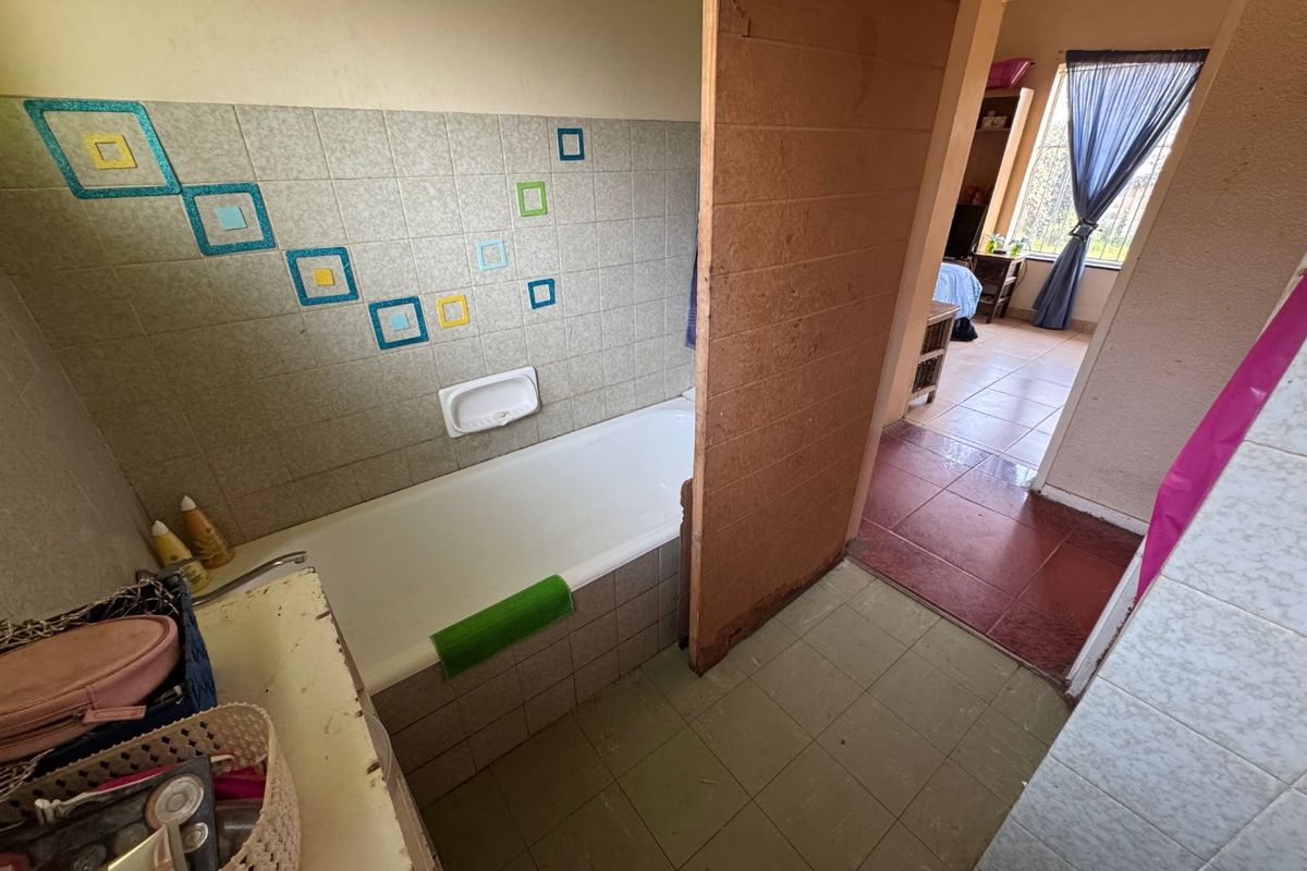 A dated bathroom featuring a built-in bathtub with tiled surround and a partial room divider, leading into an adjacent bedroom area.