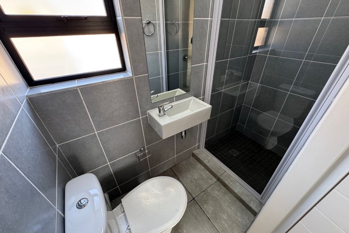 A compact, modern bathroom featuring grey floor-to-ceiling tiling, a wall-mounted basin, a toilet, and a glass-enclosed shower.