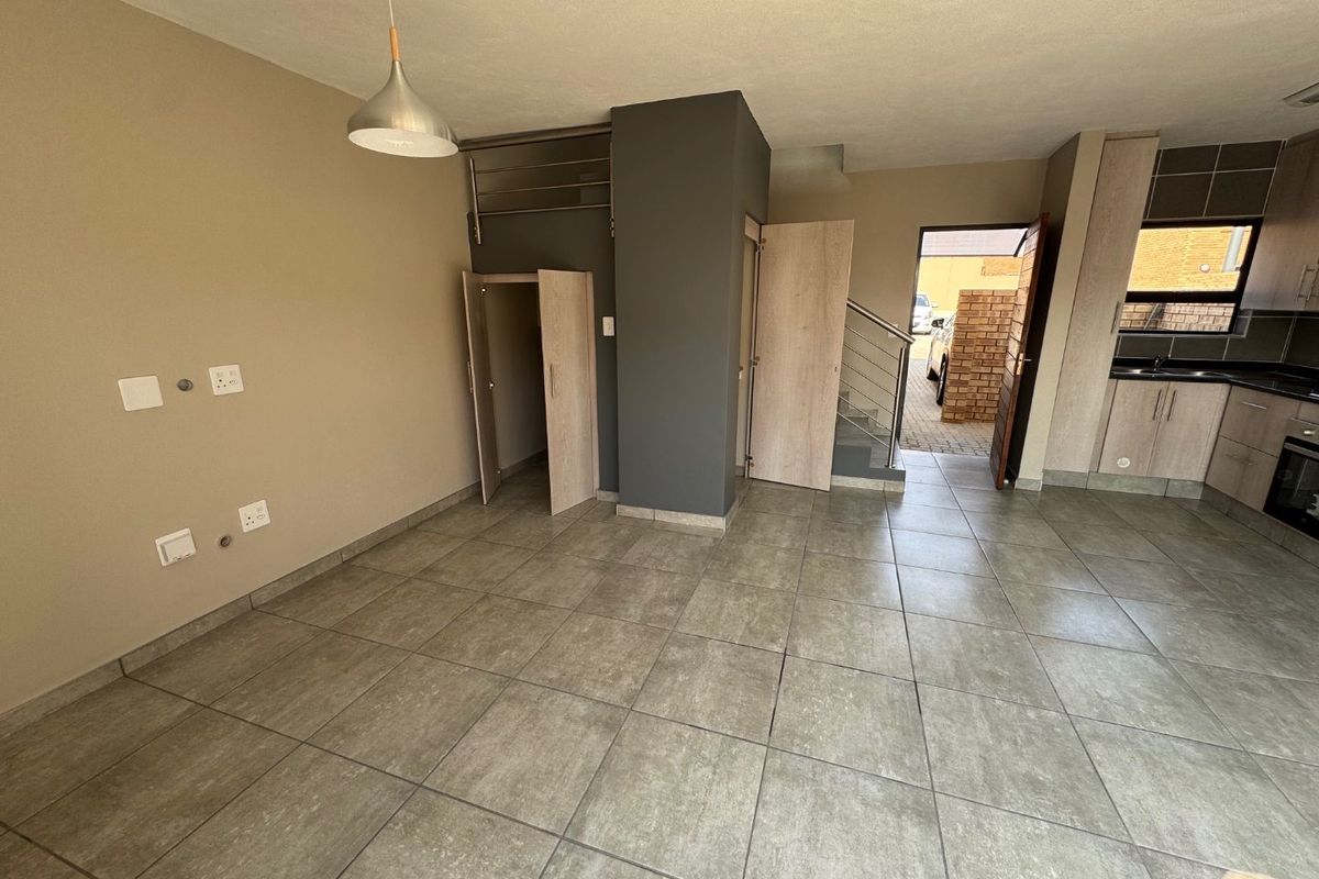 Open-plan living area featuring tiled floors, built-in storage, and a modern kitchen with integrated cabinetry, leading to an exterior entrance.